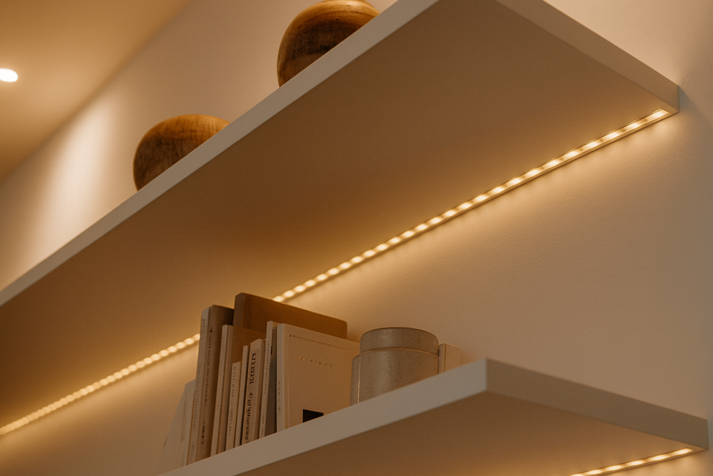 Saiba como Instalar Fita de LED: passo a passo fácil para valorizar qualquer espaço 4 Prateleiras brancas iluminadas com fita de LED embutida, decoradas com livros e objetos modernos em ambiente elegante.