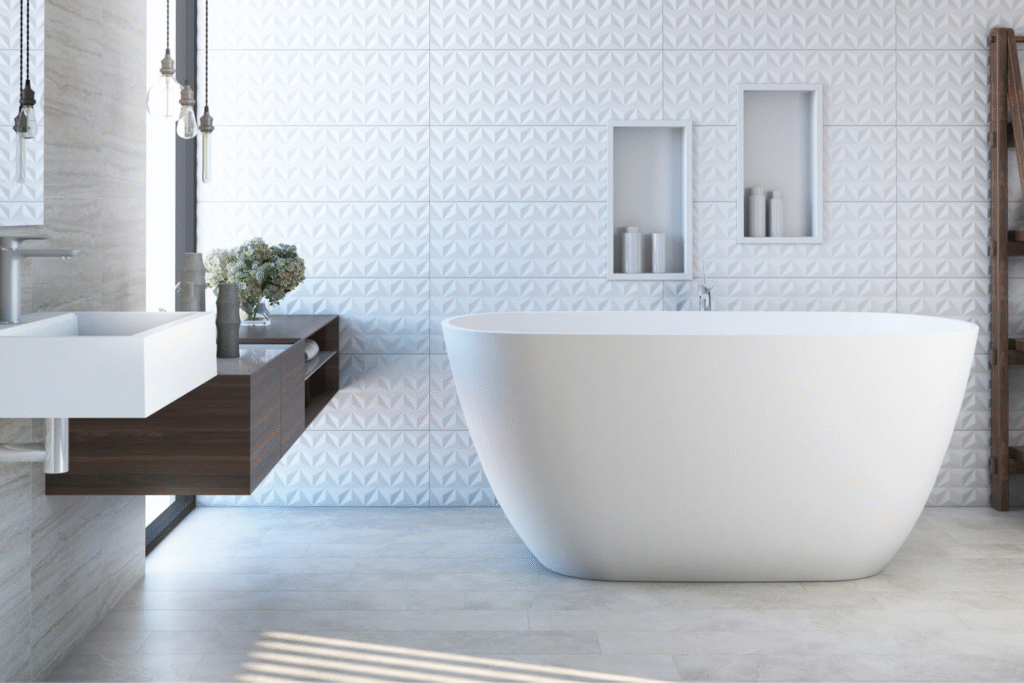 Banheira Sabbia: Conheça Modelos, Instalação e Inspirações 7 Banheiro sofisticado com banheira branca Sabbia Olinda de imersão e parede revestida em porcelanato 3D branco, criando um ambiente leve e contemporâneo.
