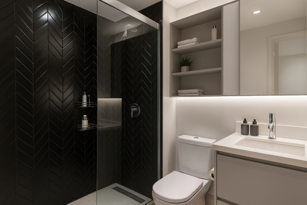 Banheiro com Pastilha Preta: Ideias, Combinações e Produtos para acertar no projeto 5 Banheiro moderno com paredes brancas, box de vidro com revestimento de pastilhas pretas em padrão “V” (chevron), chuveiro e metais cromados, bancada clara e iluminação suave.