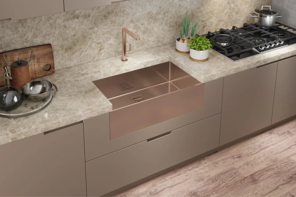 Cuba Debacco: Guia completo de modelos, Medidas e Como escolher a sua 10 Bancada marmorizada clara com cuba Debacco Primaccore rose gold de frente aparente (apron front), divisória interna, torneira rose e cooktop ao lado.